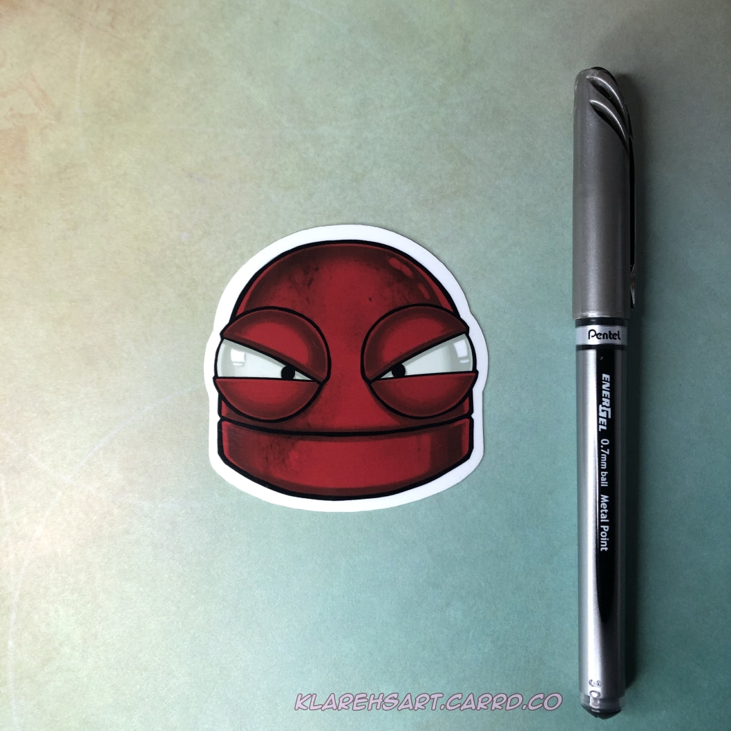 A vinyl sticker of a red robot with a mad expression. On a light gold and green background. There is an ink pen next to it for size comparison.
