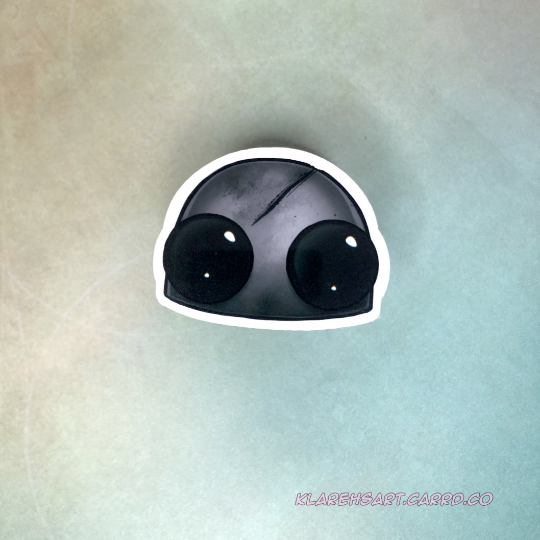 A vinyl sticker of a dead robot head. It's hull is gray and scratched, it's eyes black with no battery. On a light gold and green background.