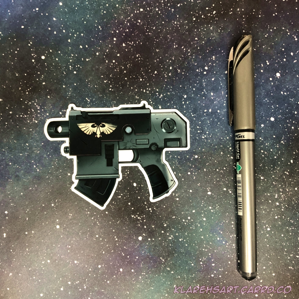 A black and green gray bolt gun pistol sticker with a futuristic theme. Roman double headed eagle adorns the side. Resting on a starry background. The ink pen next to it shows size comparison.